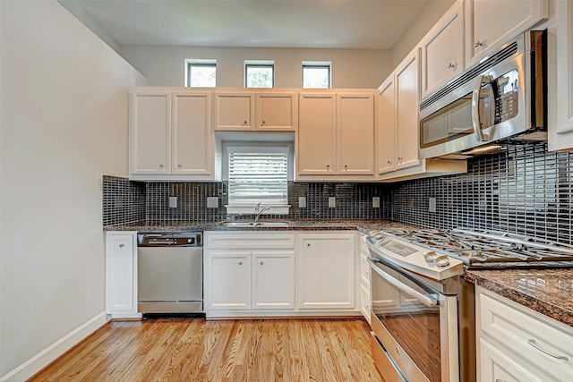 kitchen with sink, dark stone countertops, appliances with stainless steel finishes, plenty of natural light, and white cabinetry