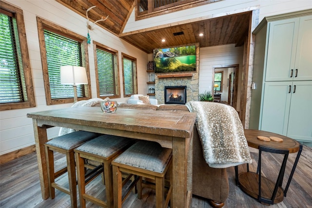 dining space with an outdoor stone fireplace, wood finished floors, wood ceiling, and wooden walls