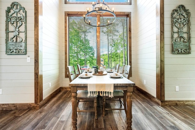 dining room with a chandelier, baseboards, dark wood finished floors, and wooden walls