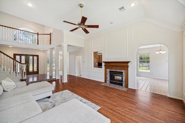 living room featuring a high end fireplace, ceiling fan with notable chandelier, crown molding, dark wood-type flooring, and high vaulted ceiling