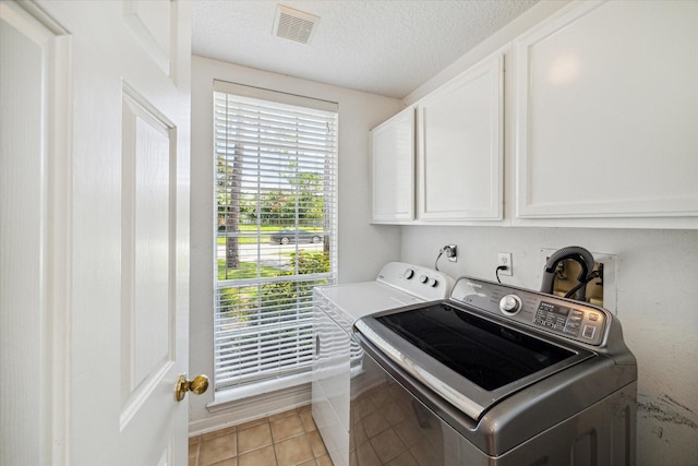 clothes washing area featuring cabinets, light tile patterned floors, a textured ceiling, and washing machine and clothes dryer