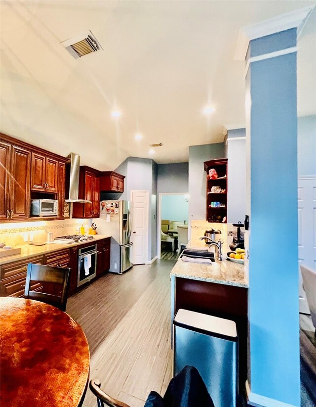 kitchen with sink, wall chimney exhaust hood, backsplash, light hardwood / wood-style floors, and appliances with stainless steel finishes