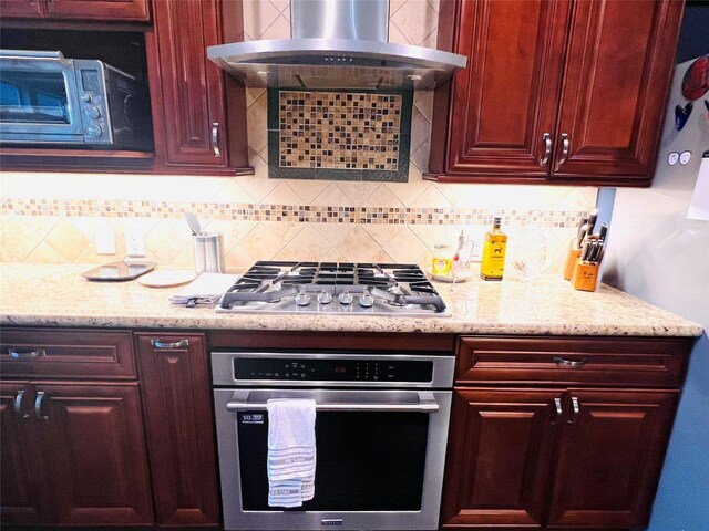 kitchen featuring decorative backsplash, exhaust hood, light stone counters, and appliances with stainless steel finishes