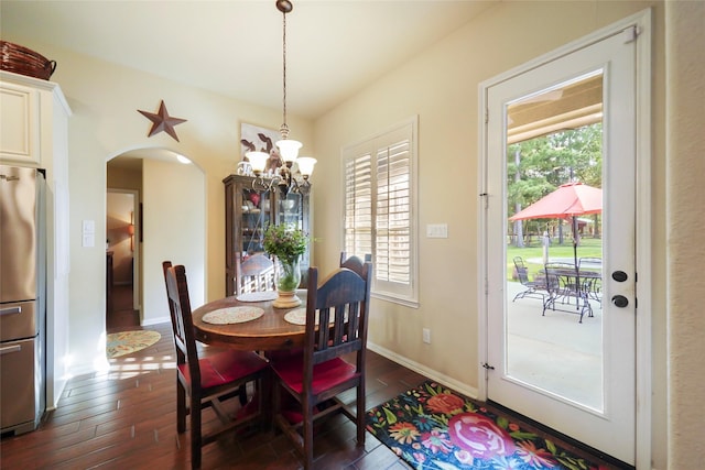 dining area with arched walkways, dark wood-style flooring, a notable chandelier, and baseboards