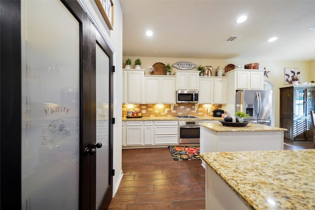 kitchen featuring tasteful backsplash, a kitchen island, appliances with stainless steel finishes, light stone countertops, and white cabinetry