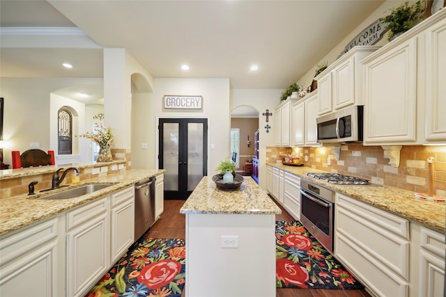 kitchen featuring tasteful backsplash, appliances with stainless steel finishes, a kitchen island, a sink, and light stone countertops