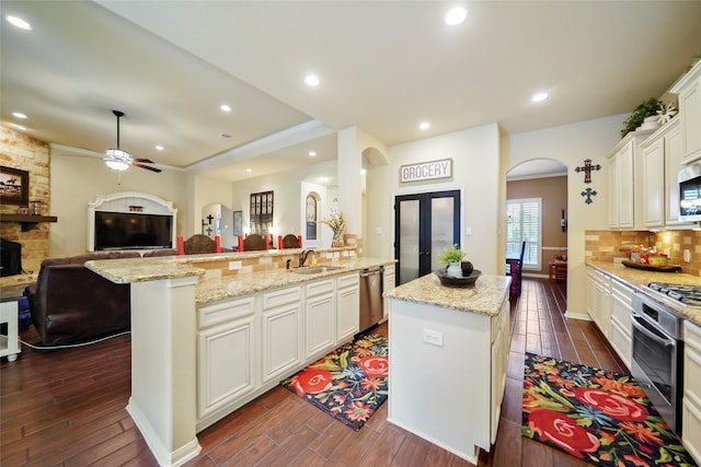 kitchen featuring appliances with stainless steel finishes, arched walkways, open floor plan, and a kitchen island with sink