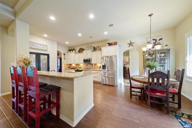 kitchen featuring arched walkways, appliances with stainless steel finishes, light stone countertops, french doors, and pendant lighting