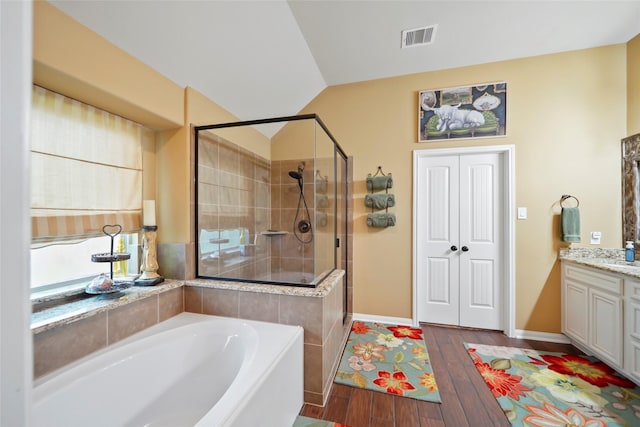 bathroom with visible vents, lofted ceiling, wood finished floors, a garden tub, and vanity