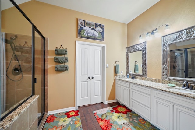 full bath featuring double vanity, wood finished floors, a sink, and a shower stall