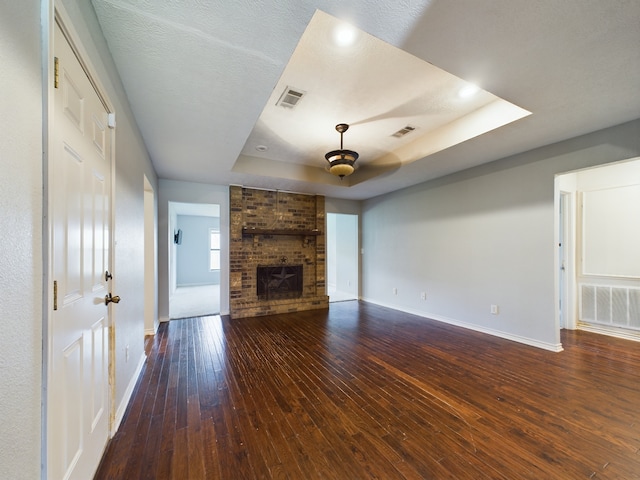 unfurnished living room featuring a fireplace, dark hardwood / wood-style flooring, and a raised ceiling