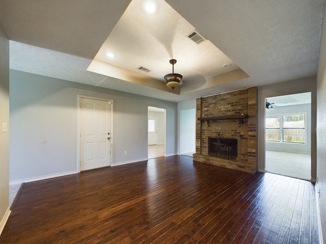 unfurnished living room featuring a brick fireplace, ceiling fan, dark wood-type flooring, and a tray ceiling