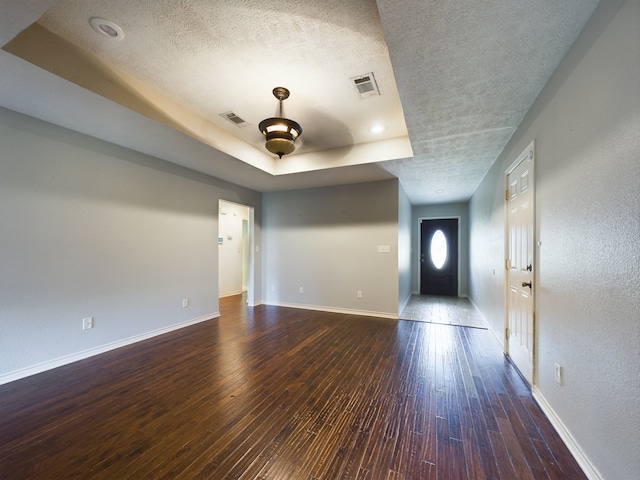 empty room with a textured ceiling, a raised ceiling, and dark wood-type flooring