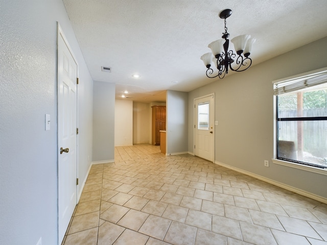 tiled spare room featuring a notable chandelier and a textured ceiling