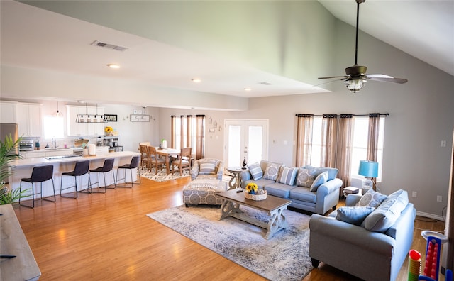 living room with ceiling fan, light hardwood / wood-style flooring, french doors, high vaulted ceiling, and sink