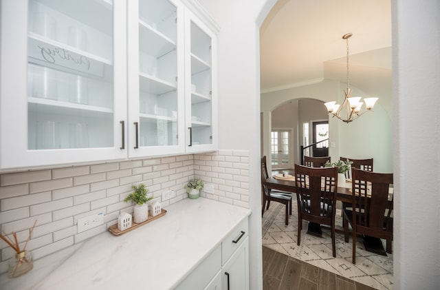 kitchen with pendant lighting, ornamental molding, white cabinetry, an inviting chandelier, and light hardwood / wood-style flooring