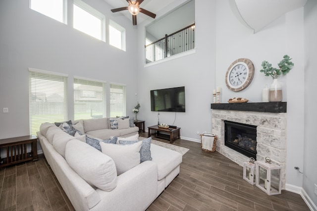 living room with ceiling fan, dark hardwood / wood-style flooring, a stone fireplace, and a high ceiling