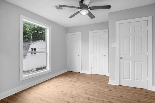 unfurnished bedroom featuring ceiling fan, multiple closets, and light wood-type flooring