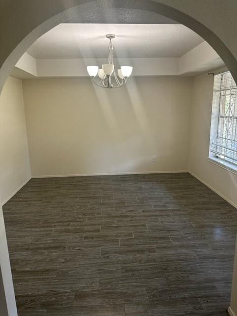 unfurnished room featuring dark wood-type flooring, a raised ceiling, and a notable chandelier