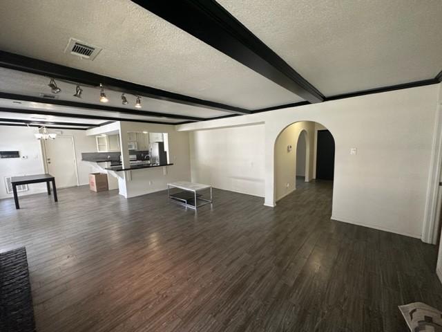 unfurnished living room featuring beam ceiling, a textured ceiling, and dark wood-type flooring