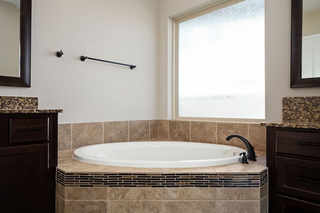 bathroom with tiled bath, plenty of natural light, and vanity