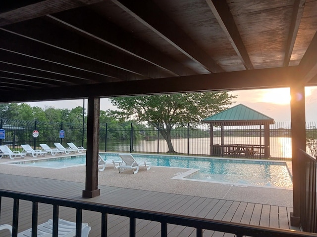 pool at dusk with a gazebo, a water view, and a patio area