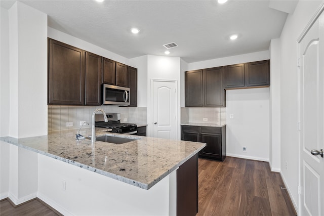 kitchen with appliances with stainless steel finishes, light stone countertops, sink, dark wood-type flooring, and kitchen peninsula