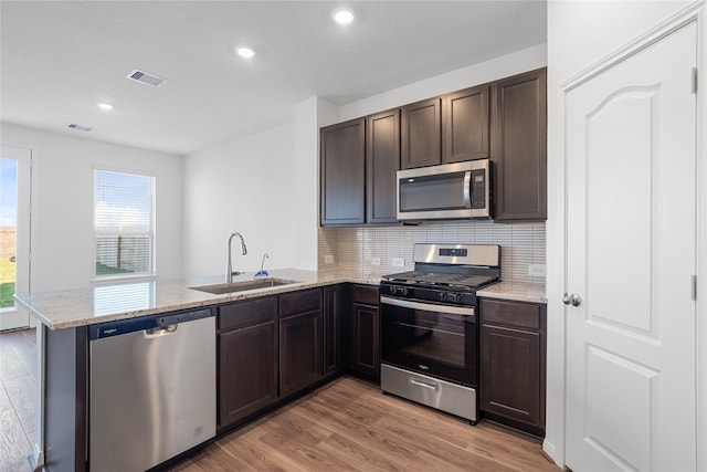 kitchen with light hardwood / wood-style floors, kitchen peninsula, sink, light stone countertops, and appliances with stainless steel finishes