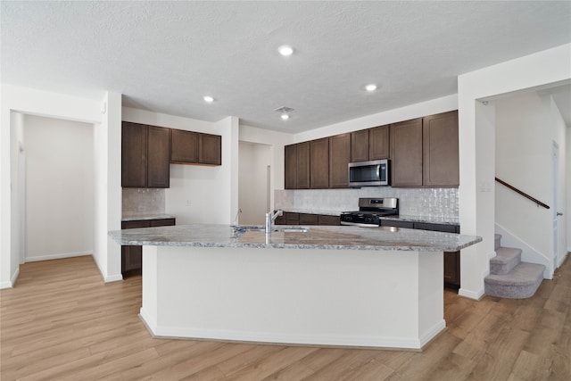 kitchen with light wood-type flooring, a textured ceiling, a kitchen island with sink, and appliances with stainless steel finishes