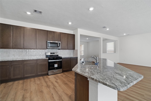 kitchen with light hardwood / wood-style floors, sink, tasteful backsplash, a kitchen island with sink, and appliances with stainless steel finishes