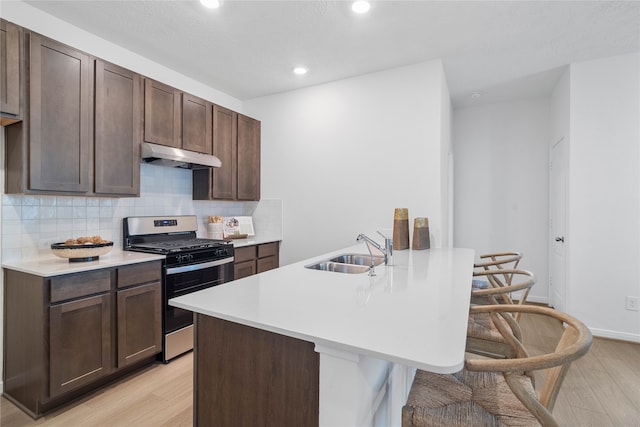 kitchen featuring tasteful backsplash, dark brown cabinets, stainless steel gas range oven, sink, and light hardwood / wood-style flooring