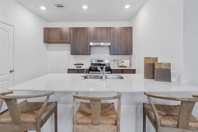 kitchen with sink, kitchen peninsula, a breakfast bar area, stainless steel gas range oven, and decorative backsplash