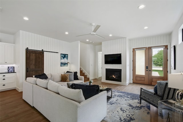 living room with light wood-type flooring, a barn door, ceiling fan, and a fireplace