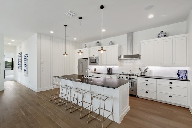 kitchen with an island with sink, dark hardwood / wood-style flooring, hanging light fixtures, high end appliances, and wall chimney exhaust hood