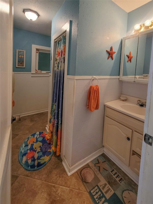 bathroom with tile patterned flooring, vanity, tile walls, and a textured ceiling