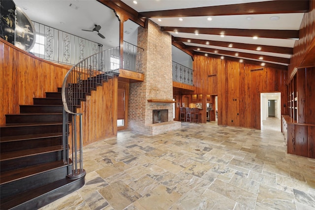 unfurnished living room featuring stone tile floors, wooden walls, a fireplace, and beam ceiling