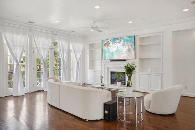 living room with dark hardwood / wood-style floors, built in shelves, ceiling fan, and ornamental molding