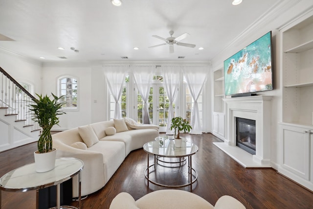 living room with ceiling fan, crown molding, built in shelves, and dark hardwood / wood-style flooring