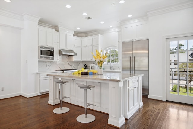 kitchen with tasteful backsplash, built in appliances, plenty of natural light, a kitchen island, and dark wood-type flooring