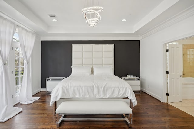 bedroom featuring a chandelier, dark hardwood / wood-style flooring, ensuite bath, and a tray ceiling