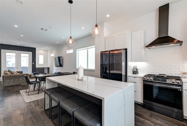 kitchen with wall chimney range hood, a center island, hanging light fixtures, and black appliances