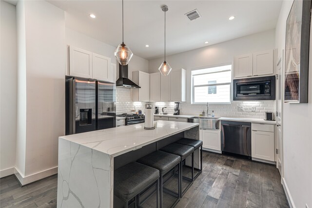 kitchen with wall chimney range hood, dark hardwood / wood-style flooring, a kitchen island, appliances with stainless steel finishes, and sink