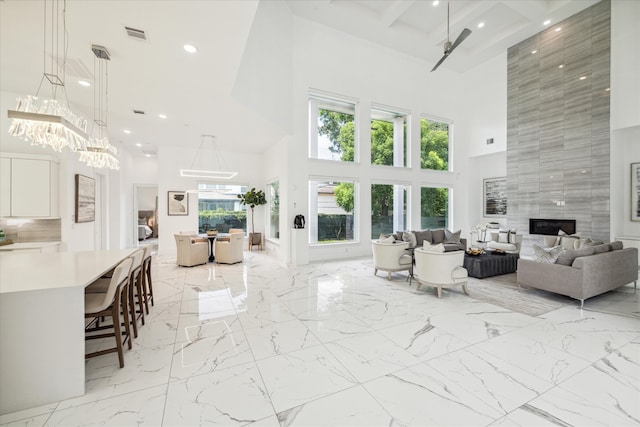 living room featuring tile walls, an inviting chandelier, light tile floors, a high ceiling, and coffered ceiling