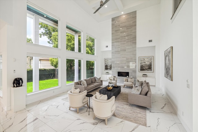 living room featuring a high ceiling, ceiling fan, a tile fireplace, and tile walls