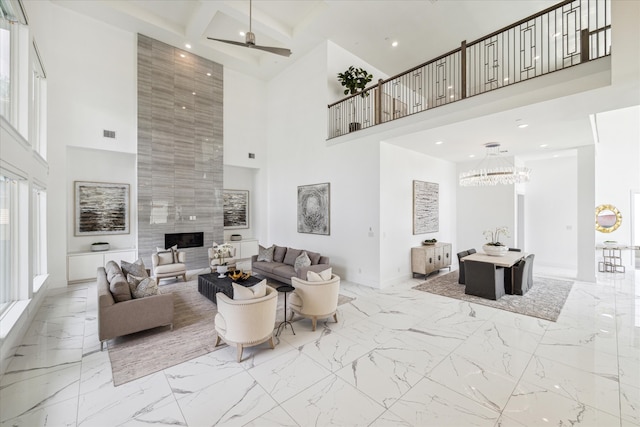 tiled living room with a high ceiling, tile walls, a fireplace, and ceiling fan with notable chandelier