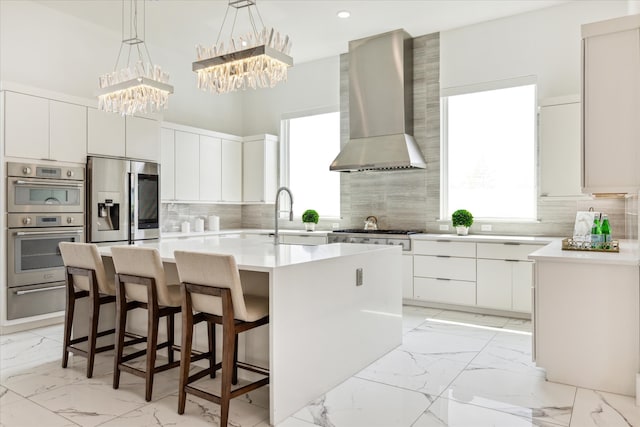 kitchen featuring appliances with stainless steel finishes, a healthy amount of sunlight, a center island, and wall chimney exhaust hood