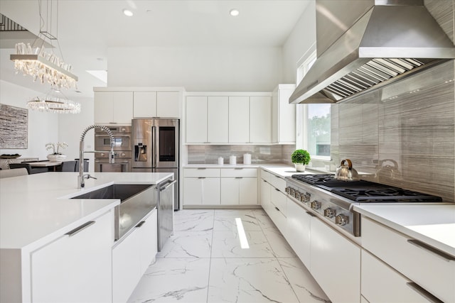 kitchen featuring backsplash, stainless steel appliances, hanging light fixtures, wall chimney exhaust hood, and white cabinets