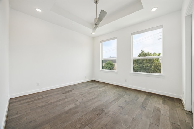 empty room featuring ceiling fan, a raised ceiling, and dark wood-type flooring