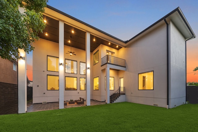 back house at dusk with a yard, ceiling fan, and a balcony