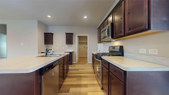 kitchen with appliances with stainless steel finishes, dark brown cabinetry, a kitchen island with sink, sink, and light hardwood / wood-style flooring